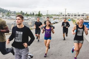 Group of men and woman running together wearing a shirt with an American flag that says train hard