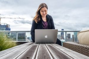 Woman using a MacBook on a bench with the view of downtown