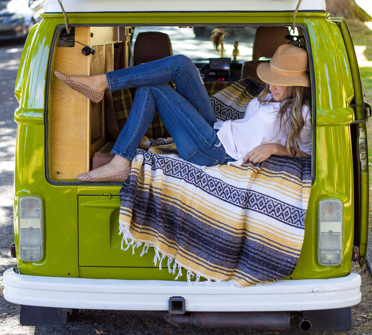 Female in hat lounges in back of lime-green VW van
