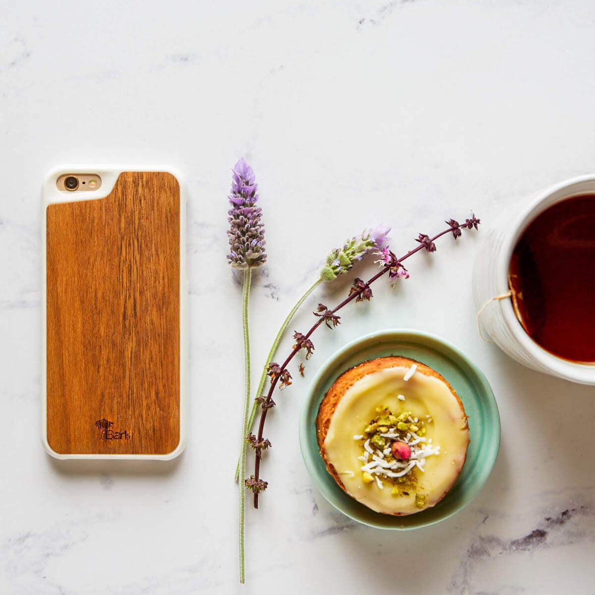 Top view of cellphone with wood cover next to a cup of tea and breakfast muffin