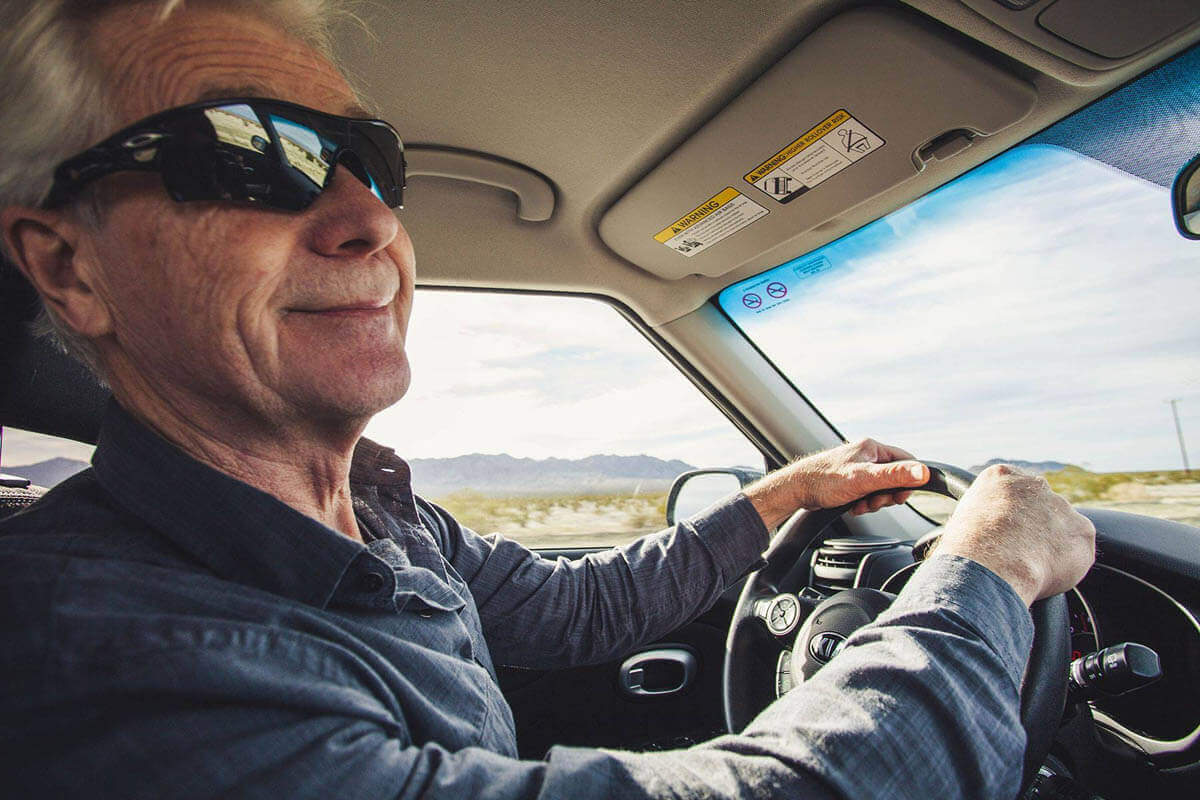 Older man in sunglasses smiles while driving through desert landscape