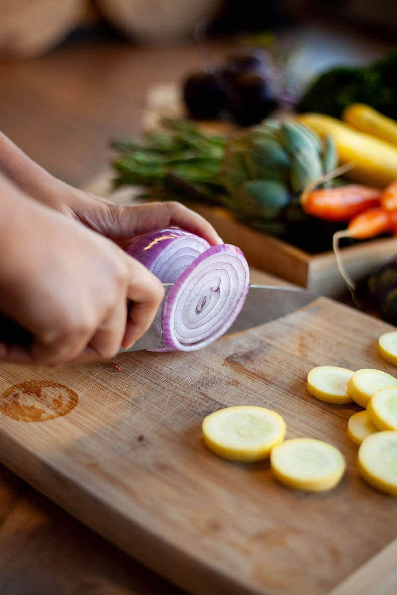 Hands slicing a red onion with knife