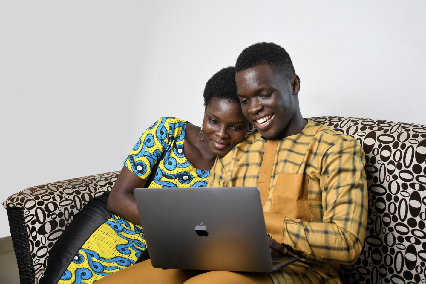african couple cuddled on couch looking at laptop