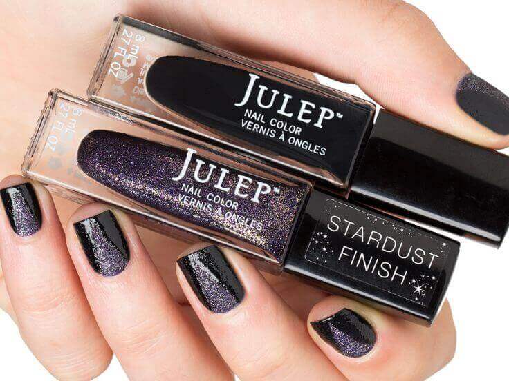 Julep nail polish in black and purple sparkles being held by a women wearing the combination of both