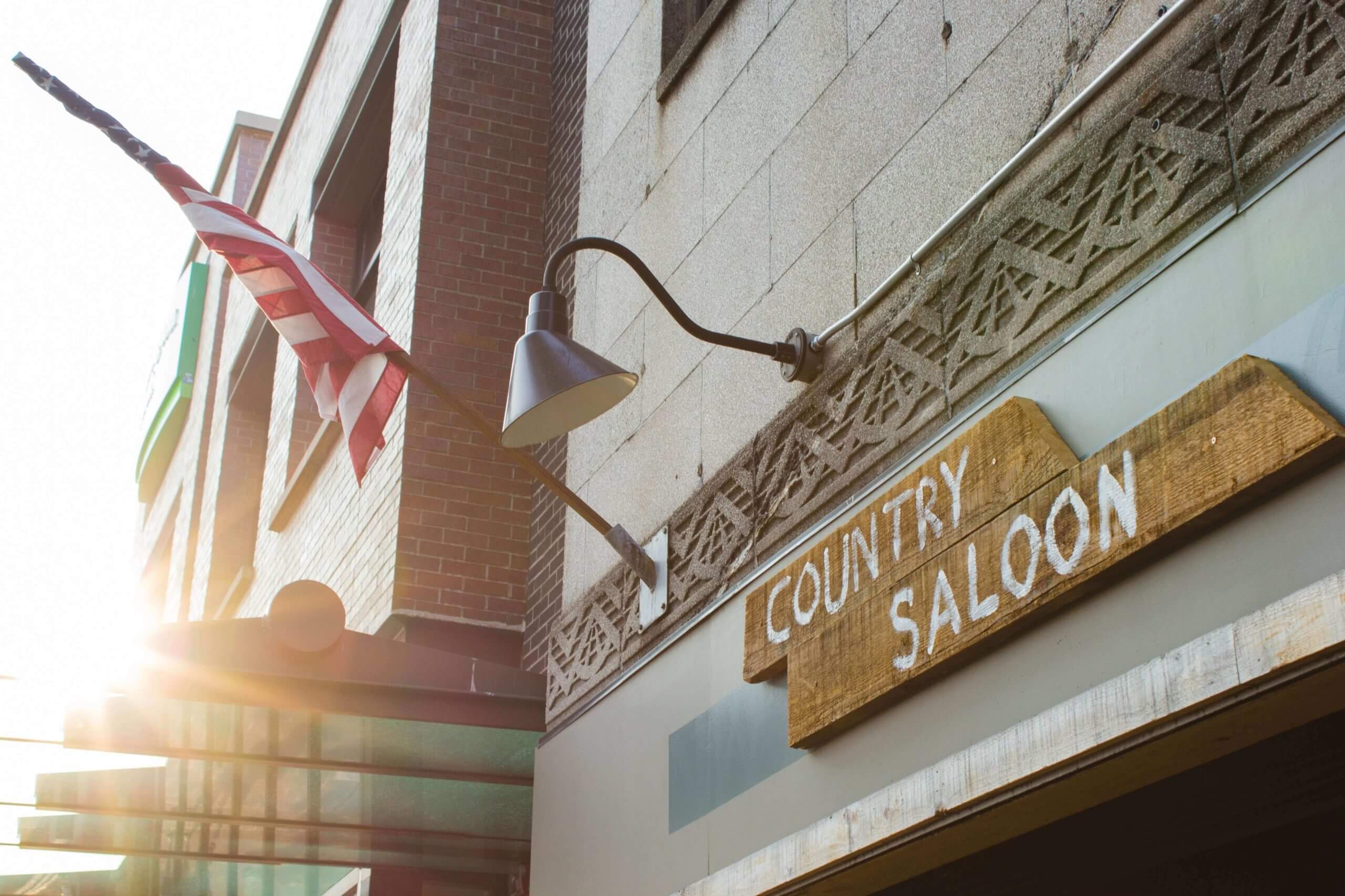 Sign that says Country Saloon on a wooden board outside a building next to an American Flag