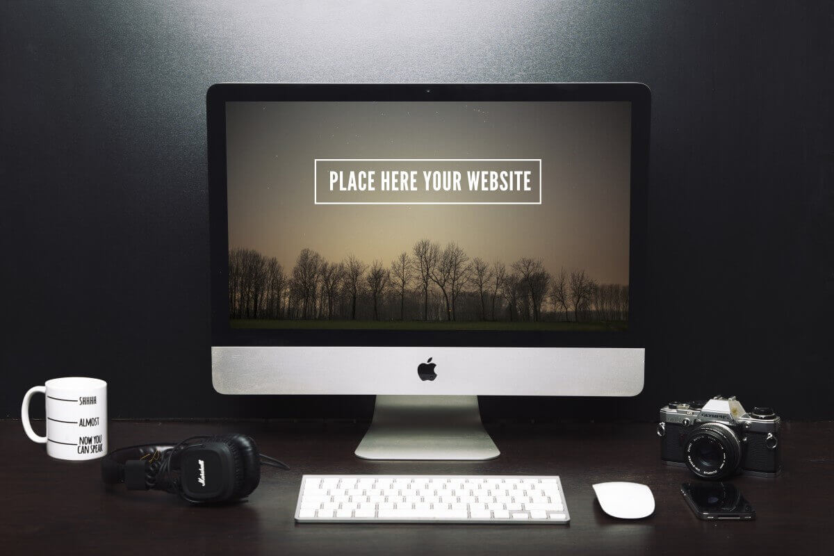 iMac that says place here your website near a coffee mug, headphones, and DSLR camera