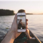 First person view of someone taking a picture of a woman sitting in a canoe through an iPhone