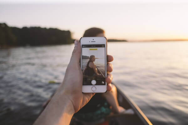 First person view of someone taking a picture of a woman sitting in a canoe through an iPhone