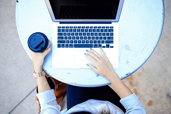 Top-down view of a woman using a MacBook while holding a cup of coffee
